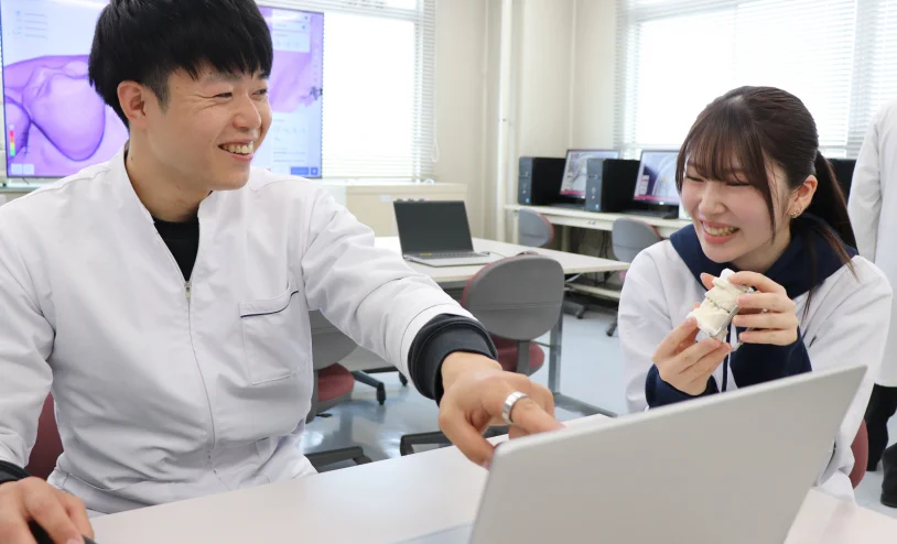 歯科技工の学習環境で模型を手にしながら説明を受ける学生の様子