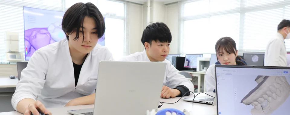 白衣姿の学生3人がノートPCで歯科のデジタルデータを確認している様子